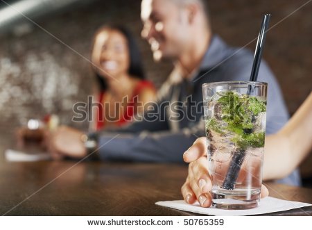 Couple sitting at bar, cocktail glass in foreground - stock photo